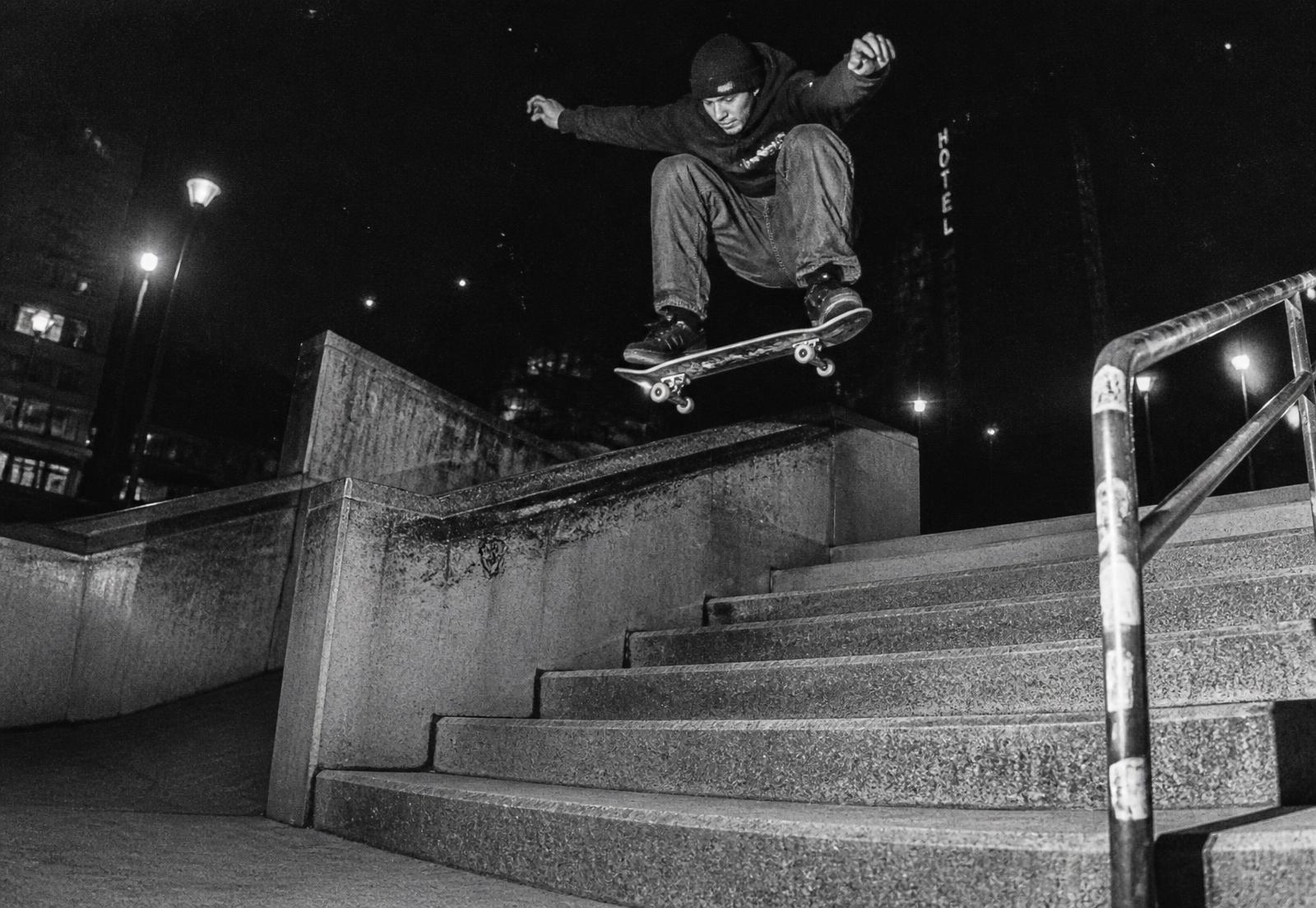 Skateboarder ollieing a concrete stair set at night under harsh flash